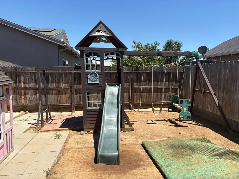 Backyard wooden playset with slide and swings before removal