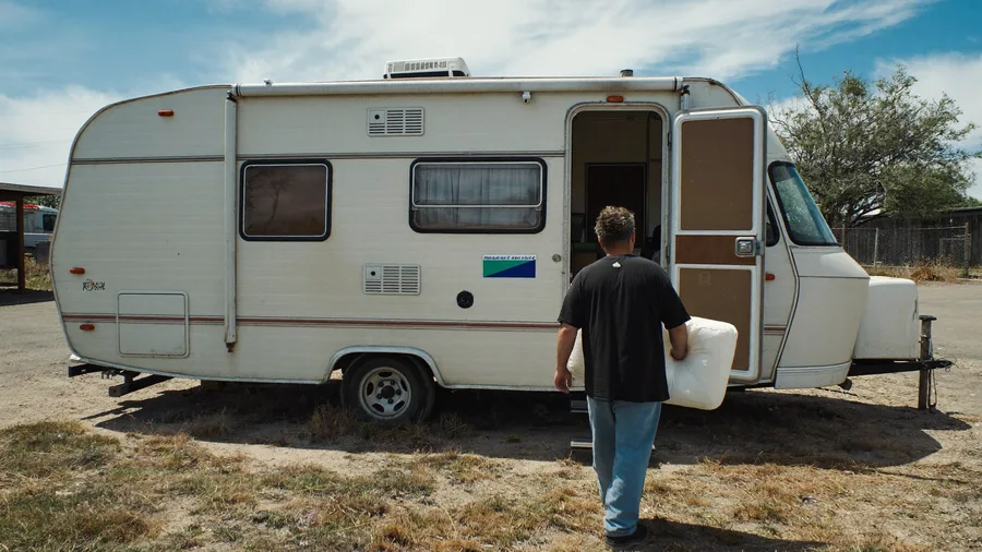 Worker pulling cushions out of an old camper trailer in a dirt side yard